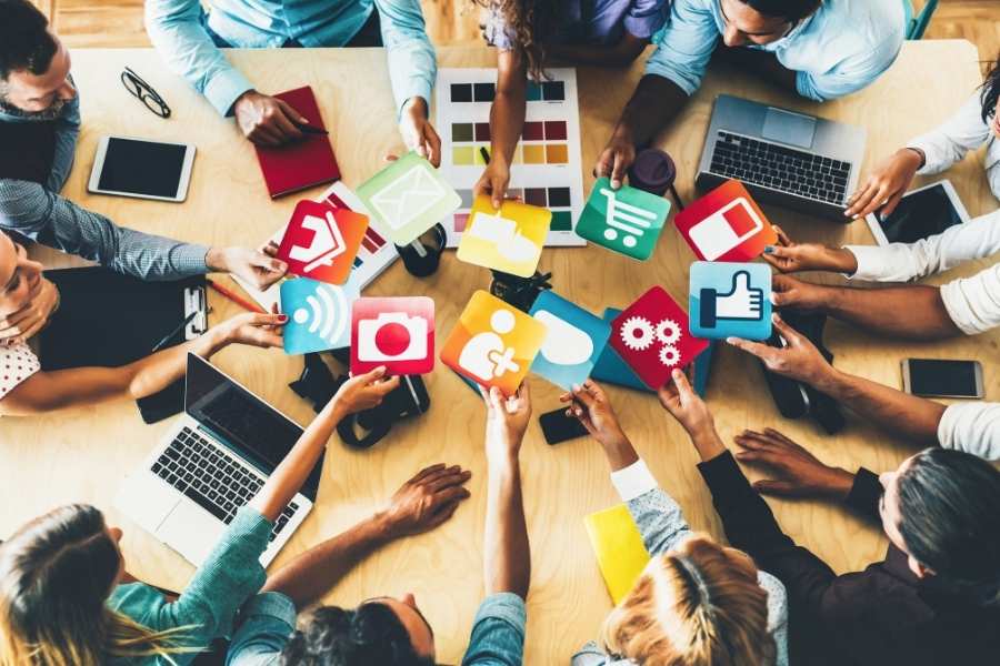 Plusieurs personnes autour d'une table tiennent des icônes colorées représentant les réseaux sociaux.