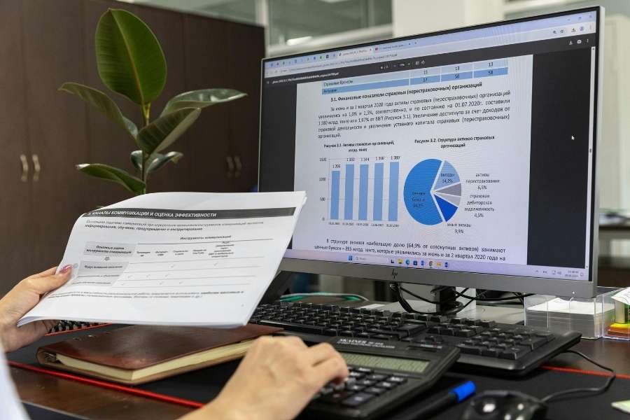 Une personne consulte des documents financiers et un écran d'ordinateur affichant des graphiques, illustrant l'analyse des données de trafic web et de performance.