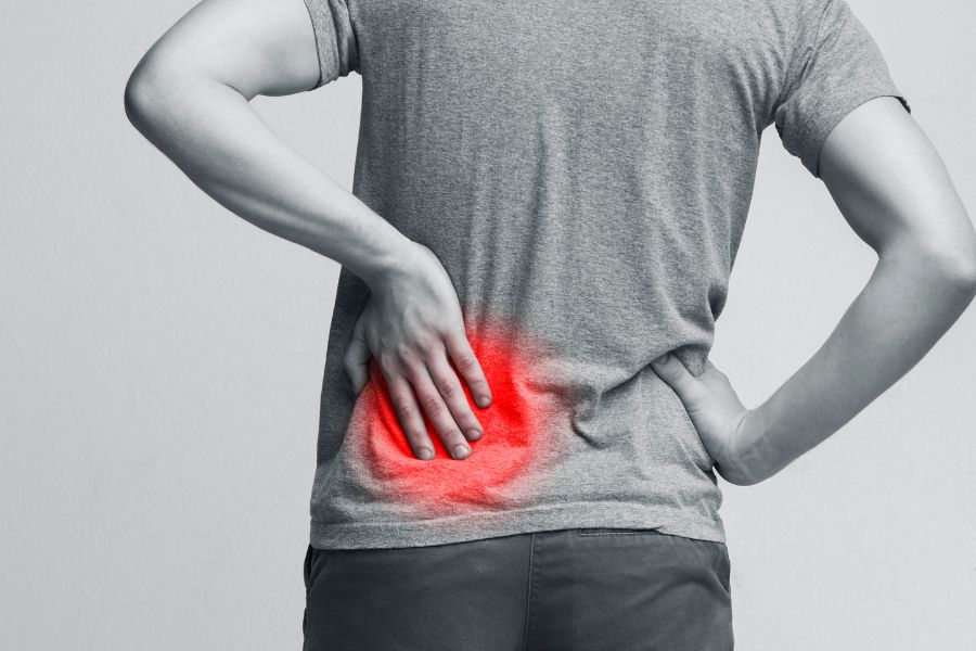 Un homme de dos se tient le bas du dos douloureux, mis en valeur par une zone rouge pour la détection précoce des maladies chroniques.